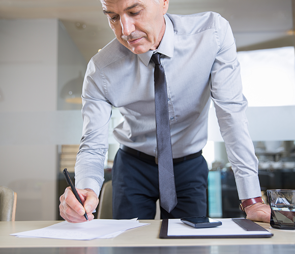 El hombre de negocios de alto nivel de flexion sobre el escritorio y escritura